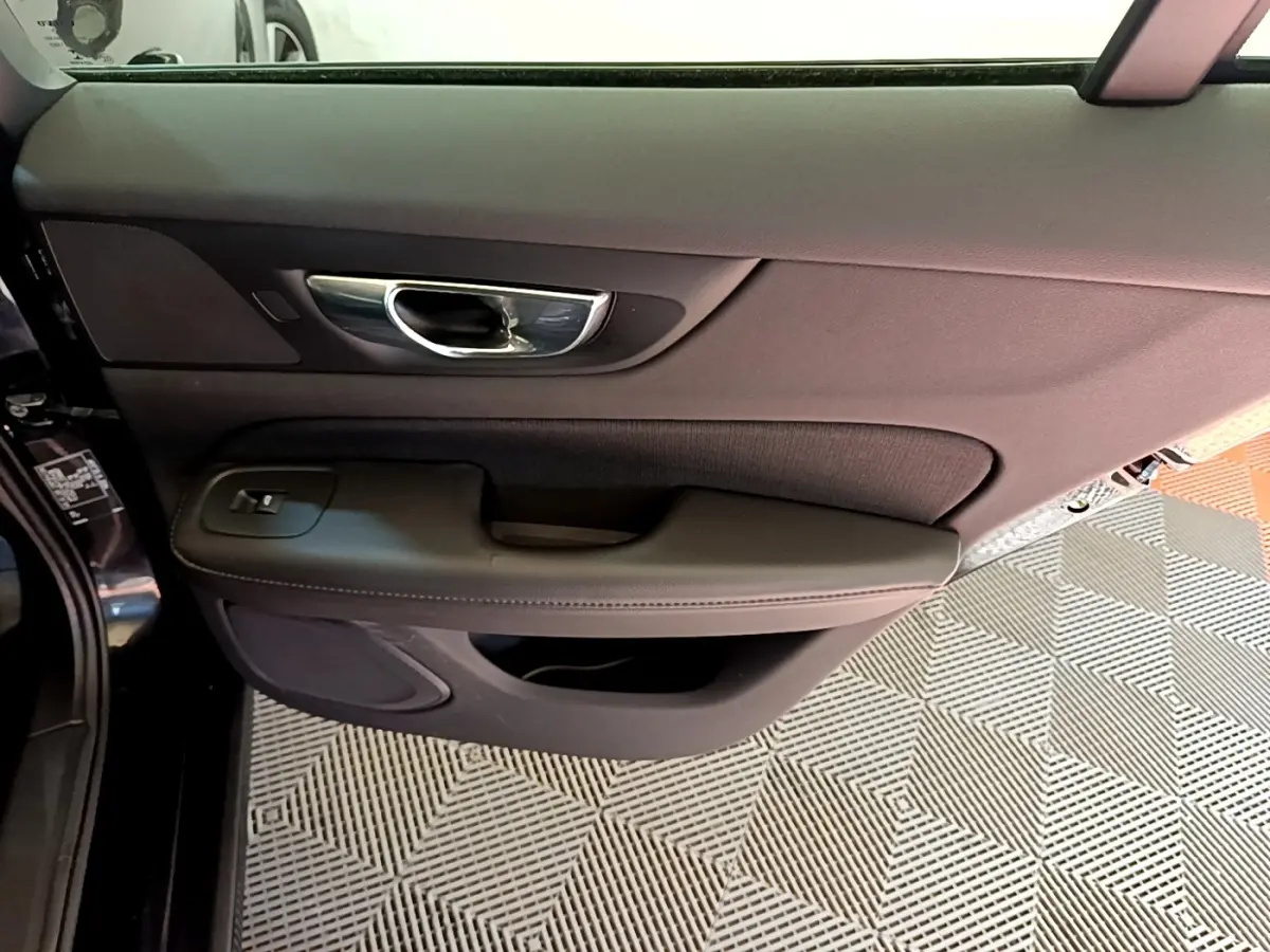 Vue intérieure côté gauche de la porte avant noire d'une Volvo V60 2020 avec poignée chrome et commandes de vitre.