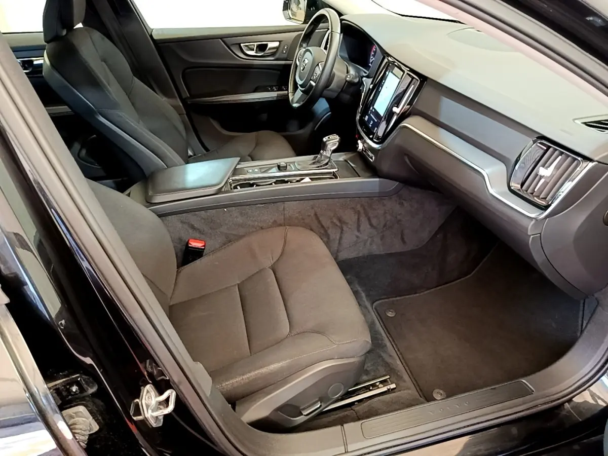Intérieur avant droit d’une Volvo V60 noire 2020, avec tableau de bord moderne et sièges tissu gris foncé.