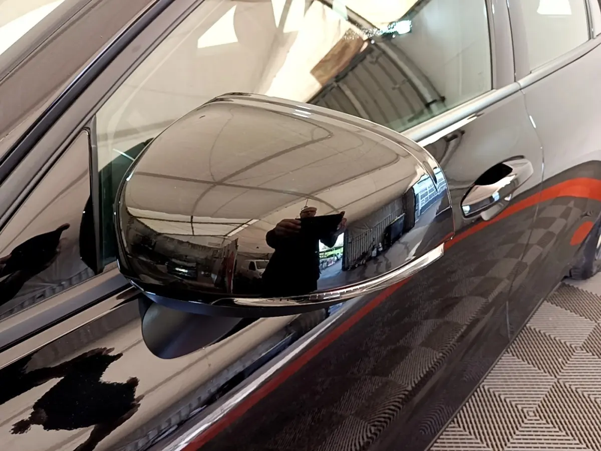 Rétroviseur côté gauche noir brillant d'une Volvo V60 D3 Business 2020 avec poignée de porte et carrosserie noire en reflet.