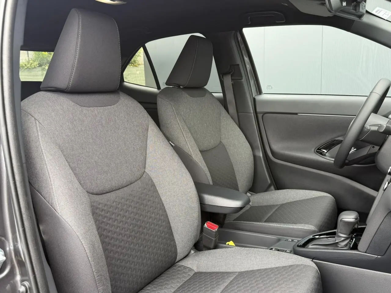 Vue intérieure côté droit montrant les sièges avant gris tissu avec accoudoir central et levier de boîte automatique Toyota Yaris Cross.