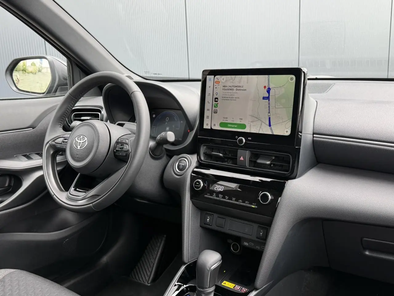 Vue intérieure côté conducteur de la Toyota Yaris Cross gris Atlas, avec écran tactile central et volant cuir.
