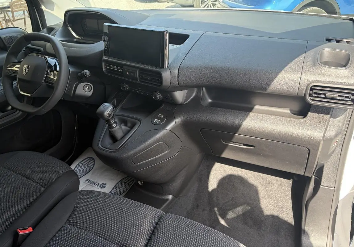 Vue intérieure côté passager du Peugeot Partner 2026, montrant tableau de bord noir avec écran tactile et levier de vitesses manuel.