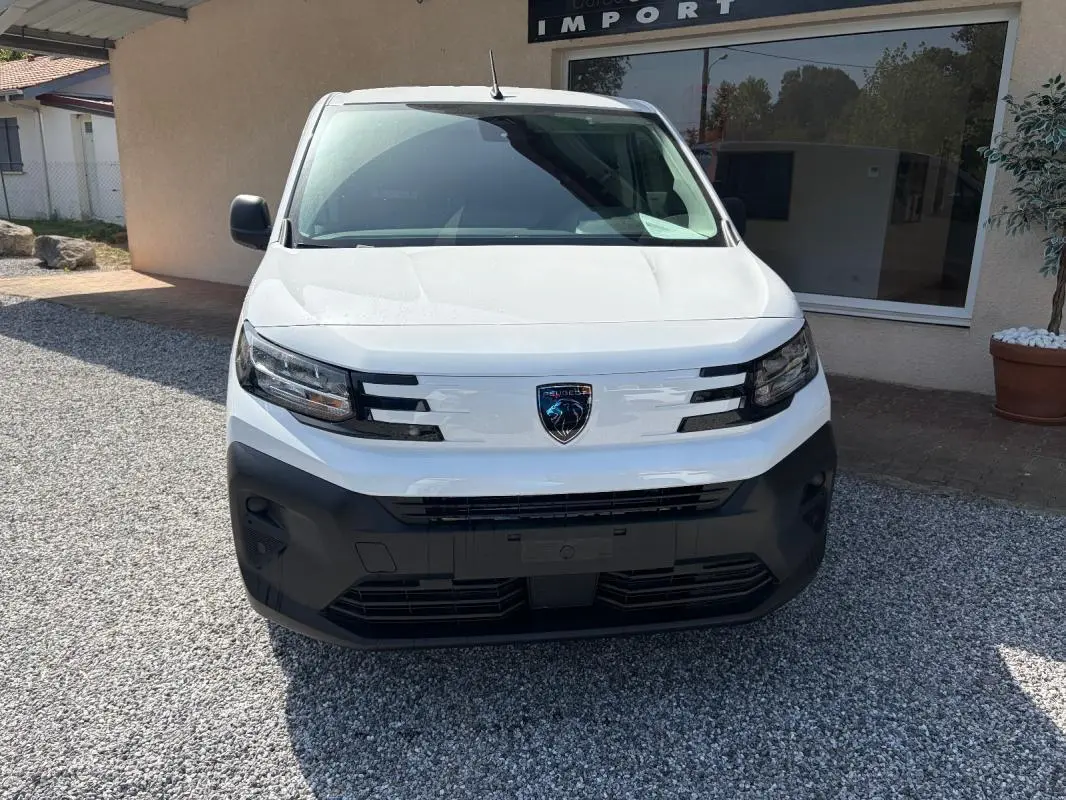 Vue frontale d’un Peugeot Partner blanc 2026 avec calandre noire et logo Peugeot central bien visible.