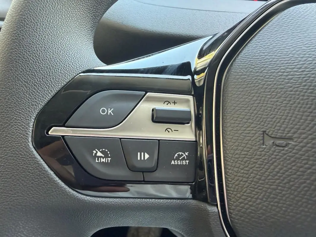 Gros plan sur les commandes à gauche du volant cuir du Peugeot Partner blanc, avec boutons limiteur et assistant de vitesse.