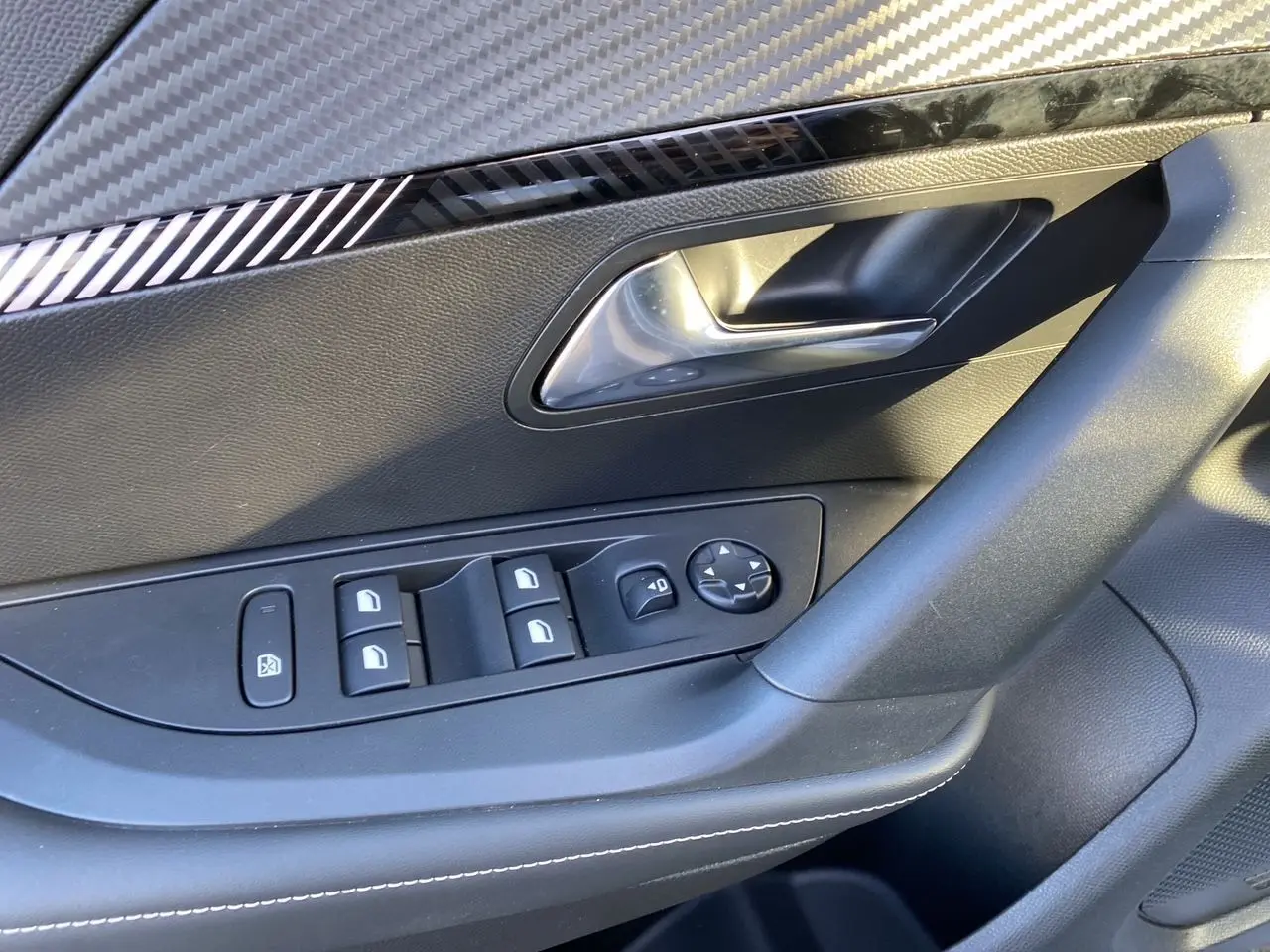 Gros plan sur la porte côté gauche du Peugeot 2008 gris Artense, montrant les commandes des vitres et la poignée intérieure chromée.