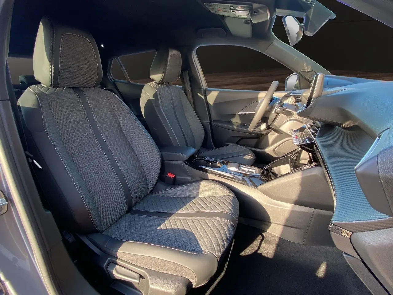 Intérieur avant du Peugeot 2008 2024 gris Artense, sièges tissu noir et console centrale brillante vue côté droit.