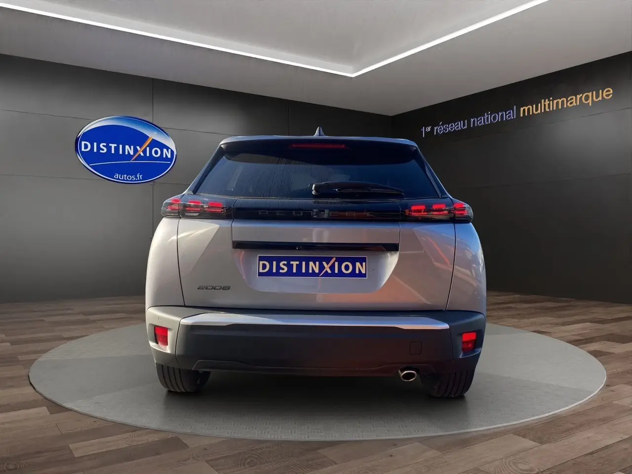 Vue arrière d'un Peugeot 2008 gris Artense 2024 avec feux LED et sortie d'échappement visible sur fond showroom.