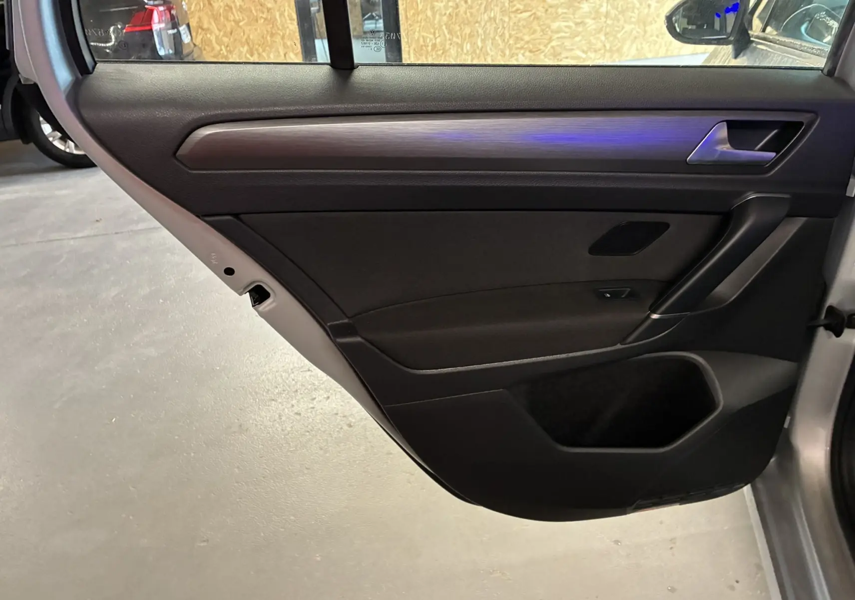 Vue intérieure côté gauche de la porte arrière d'une Volkswagen Golf Sportsvan gris avec garniture noire et insert décoratif.
