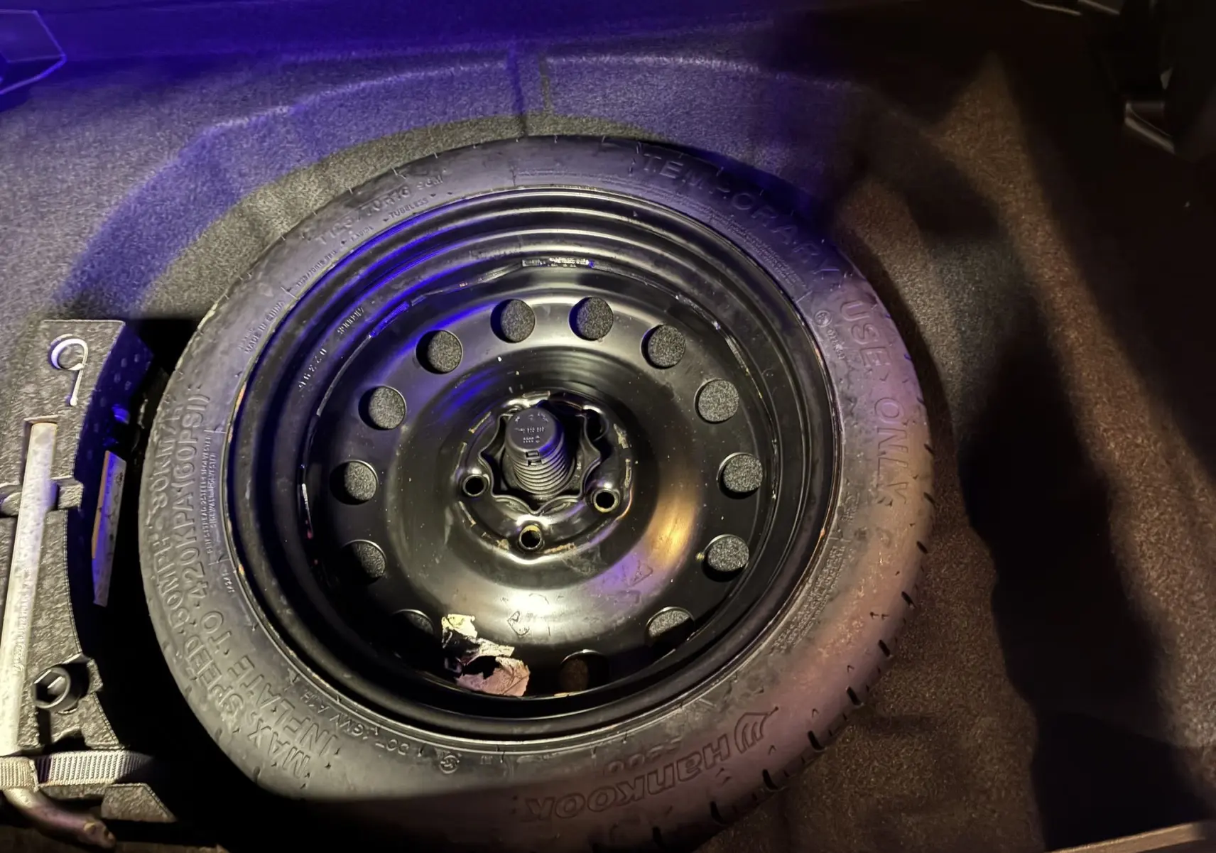 Gros plan sur la roue de secours noire dans le coffre sombre d'une Volkswagen Golf Sportsvan gris 2019.