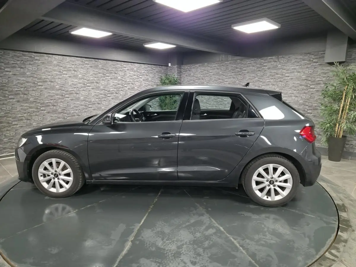 Profil côté gauche d'une Audi A1 Sportback gris Manhattan 2024 avec jantes argentées en intérieur showroom.