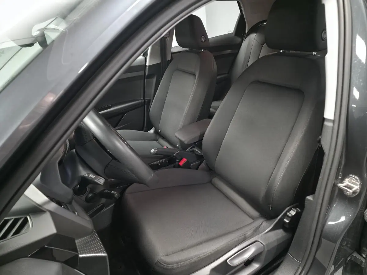 Vue intérieure côté conducteur de l'Audi A1 Sportback 2024 gris Manhattan, sièges sport en tissu Novum et accoudoir central.