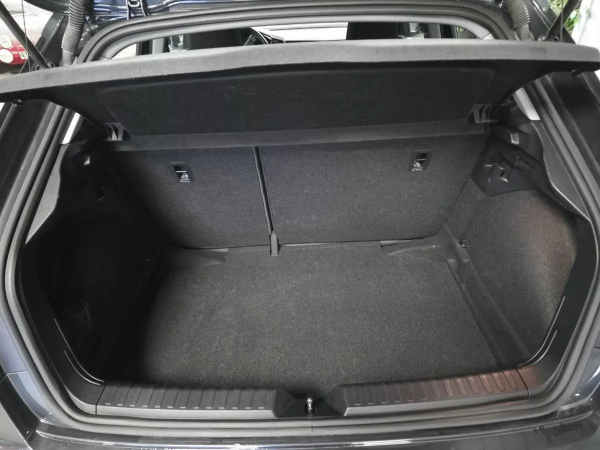 Coffre ouvert vu de l'arrière d'une Audi A1 Sportback gris Manhattan, espace de chargement vide et tapis noir.