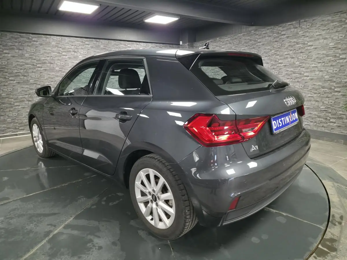Audi A1 Sportback gris Manhattan vue 3/4 arrière droit avec feux LED et jantes argentées en intérieur showroom.