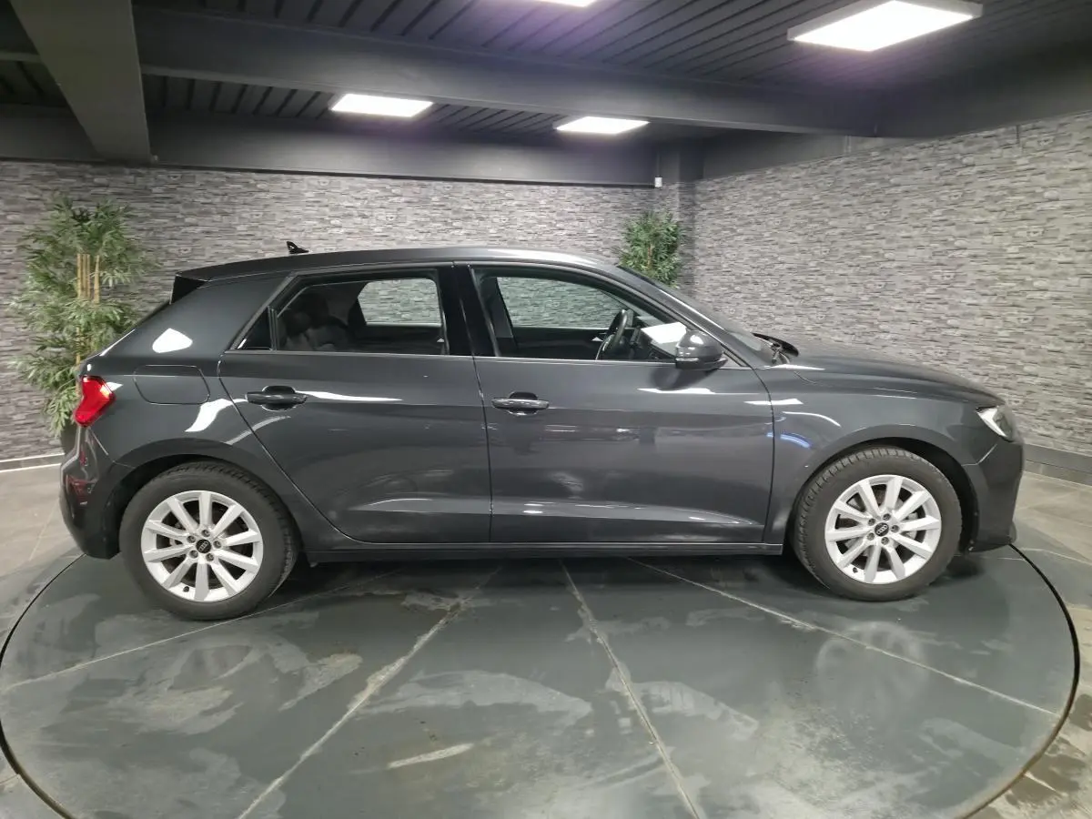 Profil côté gauche d'une Audi A1 Sportback 2024 gris Manhattan avec jantes argentées en intérieur showroom.