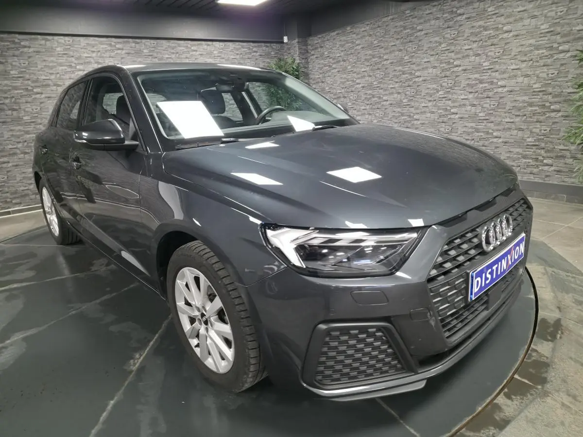 Audi A1 Sportback gris Manhattan vue 3/4 avant droit avec calandre noire et phares LED dans un showroom.