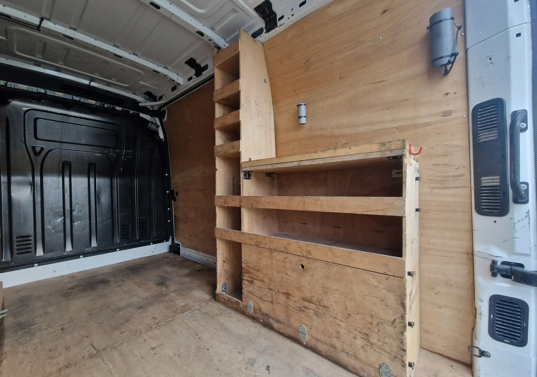 Intérieur du Renault Master blanc vu de l'arrière droit, montrant l'aménagement bois avec étagères et rangements.