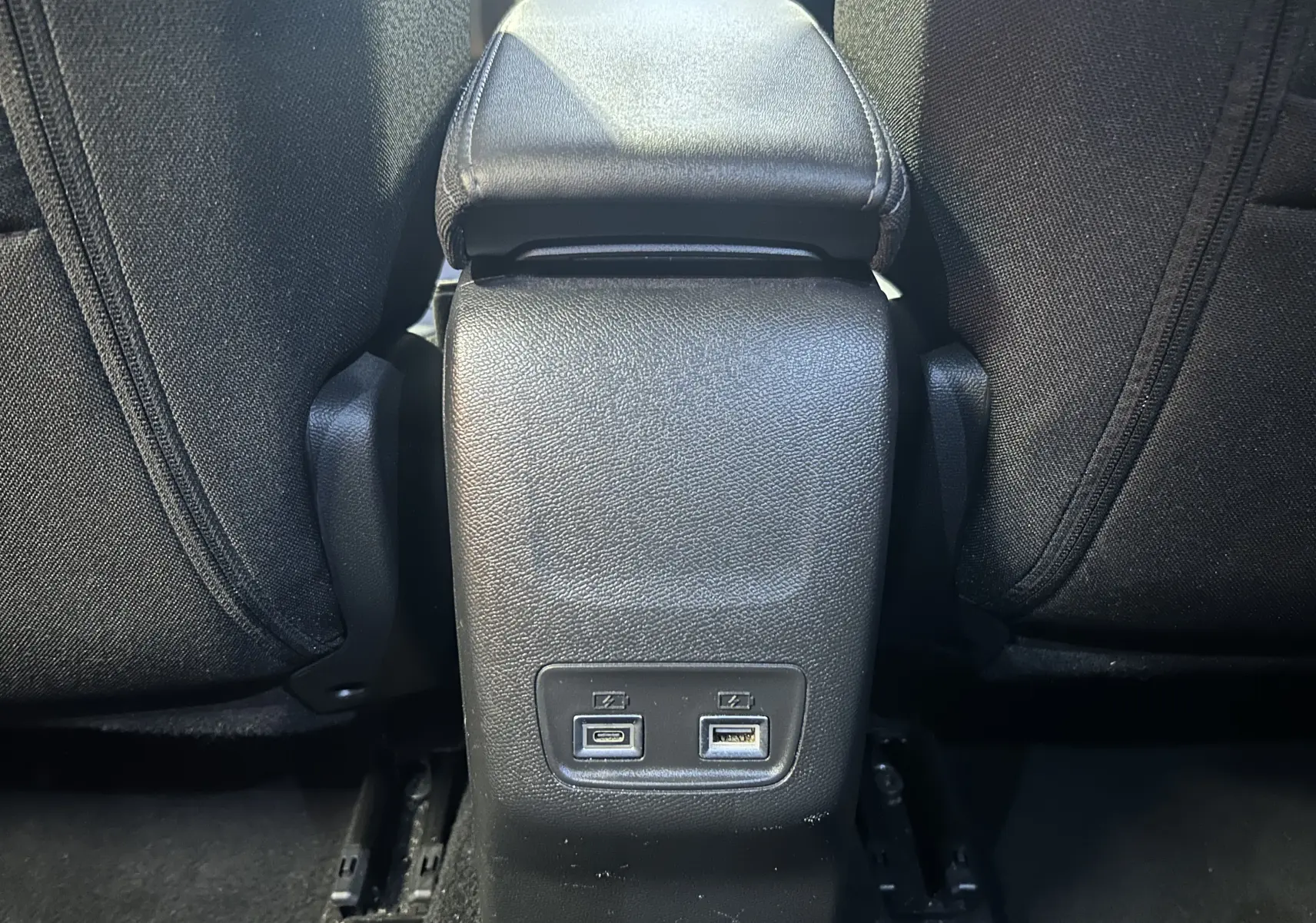 Vue rapprochée de la console centrale arrière du Peugeot 2008 Allure Hybrid 145, avec ports USB visibles entre les sièges noirs.