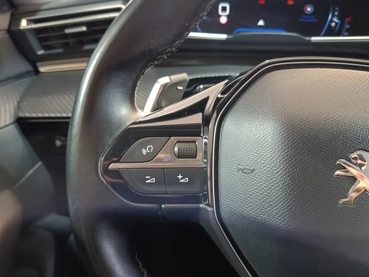 Gros plan sur le volant cuir noir de la Peugeot 508 gris clair, avec commandes vocales et volume intégrées.