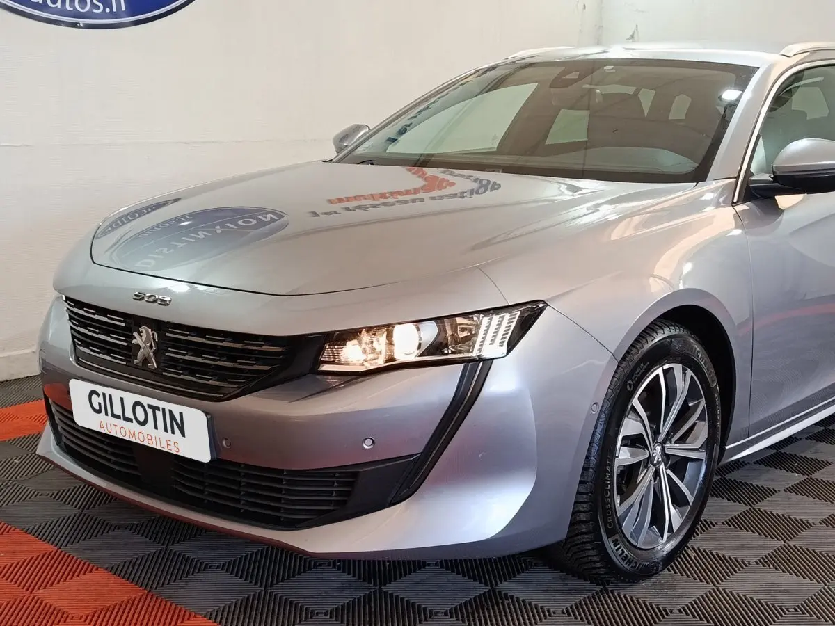 Vue 3/4 avant droit d'une Peugeot 508 gris clair avec phares allumés et jantes alliage distinctives.