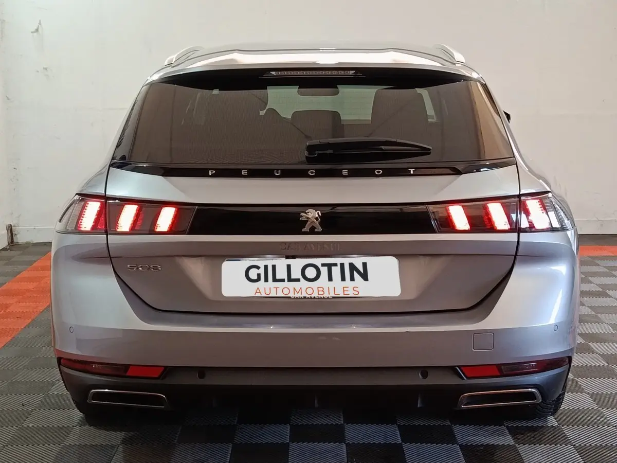 Vue arrière d'une Peugeot 508 gris clair avec feux LED allumés dans un intérieur de garage.