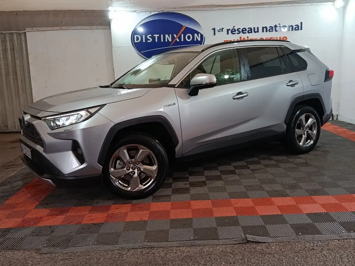 Toyota RAV4 Hybride gris clair vu de profil droit en intérieur, avec jantes alliage et logo Distinxion en arrière-plan.