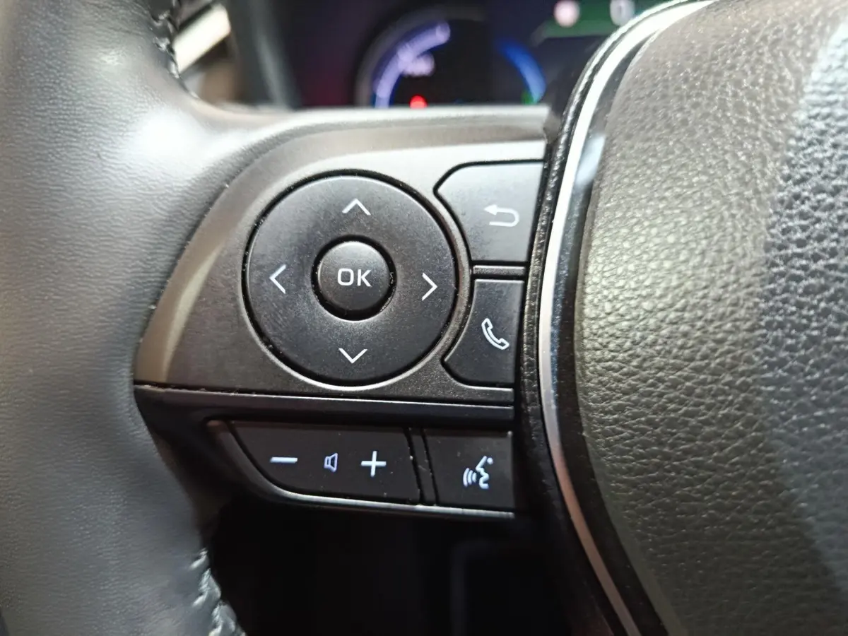 Gros plan sur les commandes multifonctions noires à gauche du volant cuir du Toyota RAV4 hybride 2021.