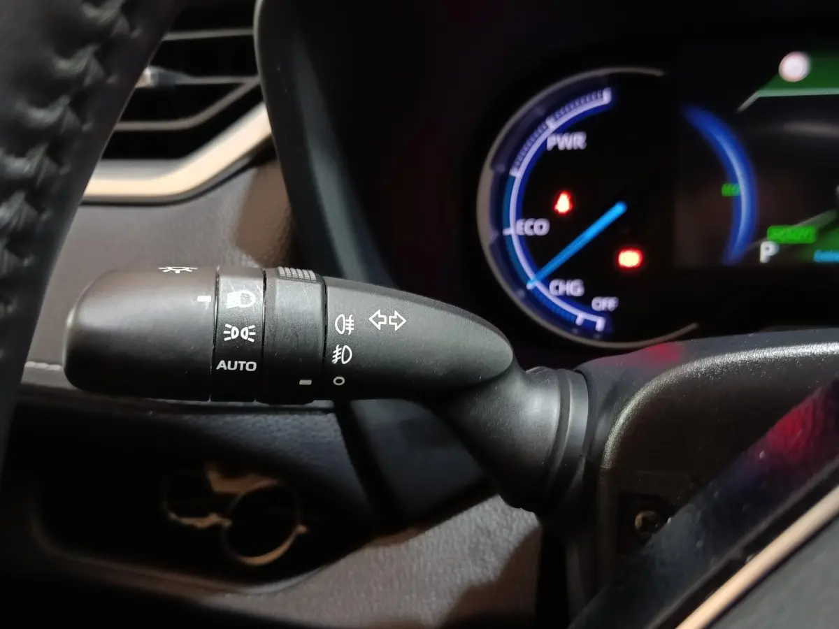 Gros plan sur la commande des phares et clignotants du Toyota RAV4 Hybride 2WD, avec tableau de bord numérique en arrière-plan.