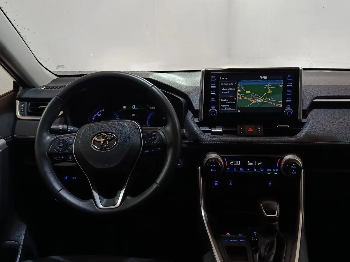 Vue intérieure du tableau de bord du Toyota RAV4 Hybride 2021, avec volant cuir et écran tactile central allumé.