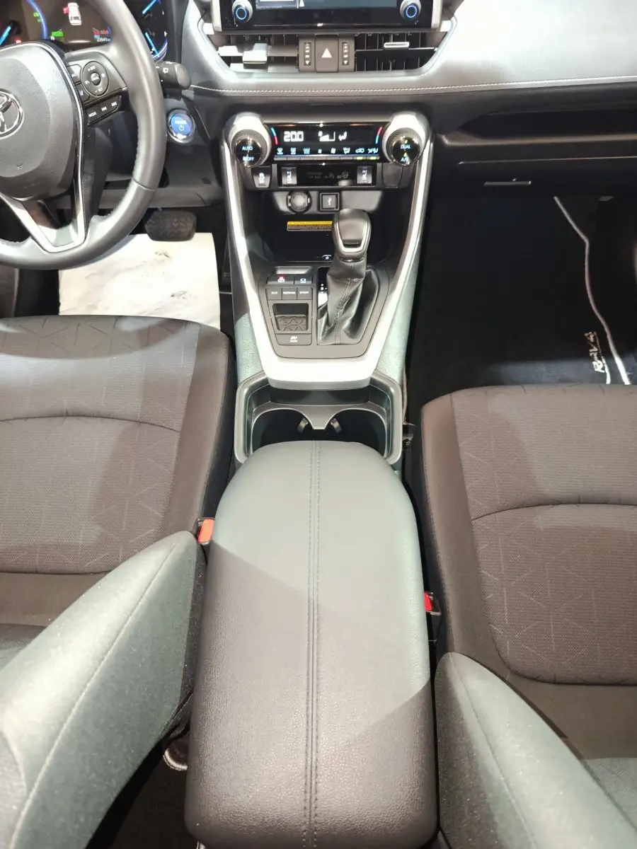 Vue intérieure centrée sur la console centrale noire du Toyota RAV4 hybride avec sièges tissu foncé et volant partiel.