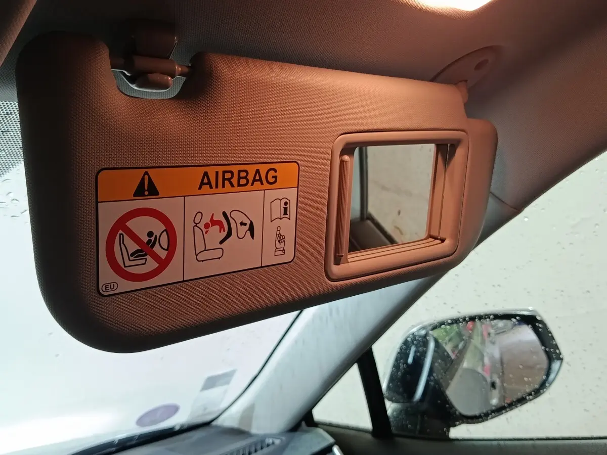 Vue intérieure du pare-soleil côté conducteur beige avec miroir et avertissement airbag, rétroviseur extérieur visible.