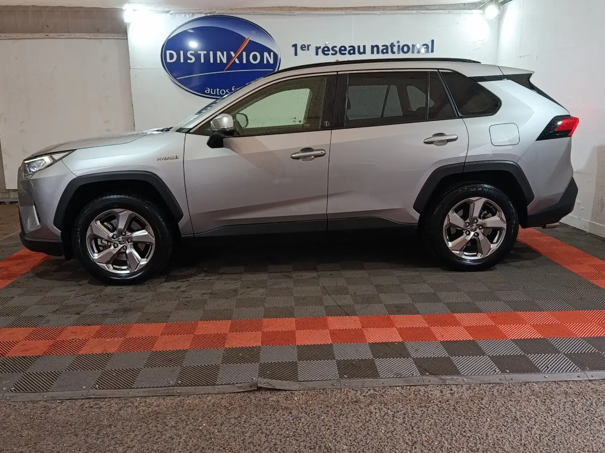 Profil droit d'un Toyota RAV4 hybride 2WD gris clair, avec jantes alliage et détails noirs autour des passages de roues.