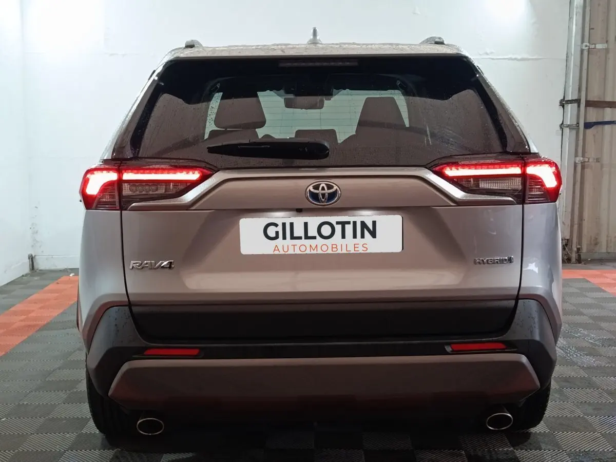 Vue arrière du Toyota RAV4 hybride gris avec feux LED allumés dans un garage fermé.