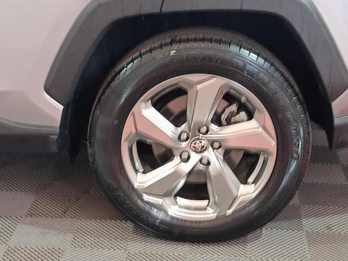 Gros plan sur la roue avant droite du Toyota RAV4 hybride 2021 avec jante alliage argentée et carrosserie claire.