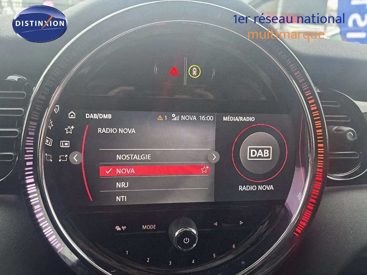 Affichage du système multimédia MINI 2023 en gros plan, avec sélection de la radio Nova sur écran circulaire lumineux.