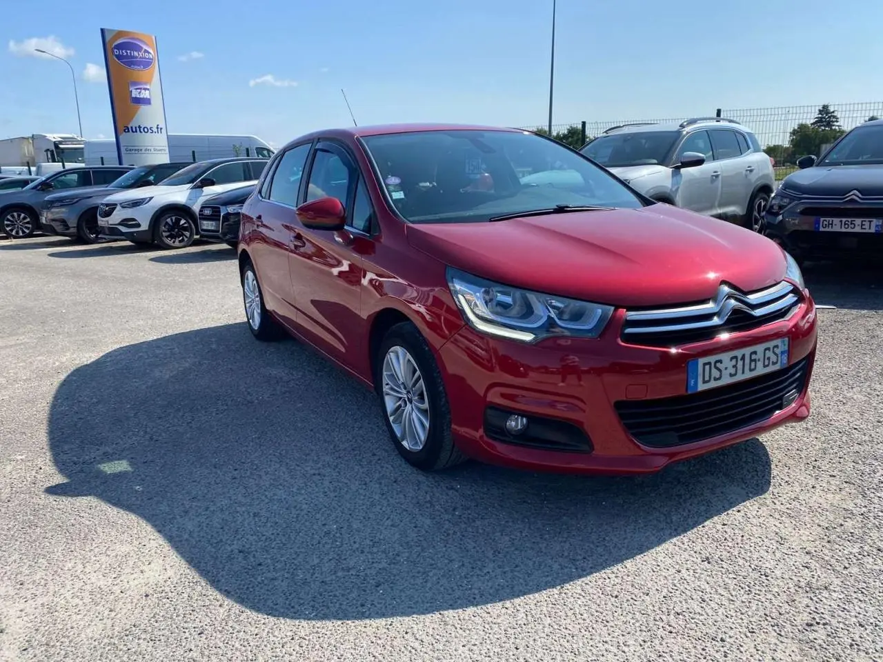 Citroën C4 rouge métallisé vue 3/4 avant droit sur parking avec projecteurs antibrouillard et calandre chromée.