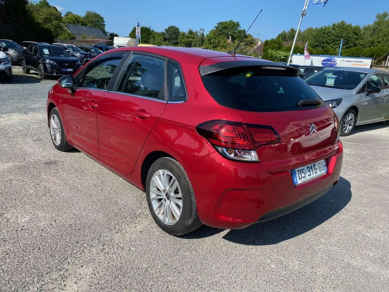 Citroën C4 rouge métallisé vue 3/4 arrière côté gauche, avec feux arrière et lunette teintée visibles.