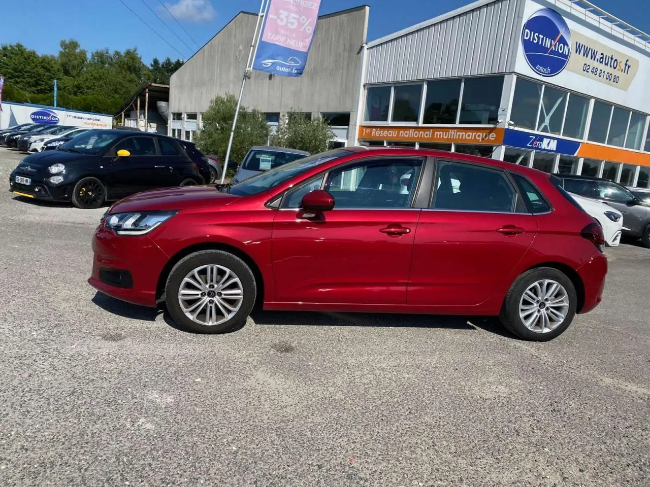 Profil latéral gauche d'une Citroën C4 rouge métallisée de 2015, garée devant un concessionnaire multimarque.