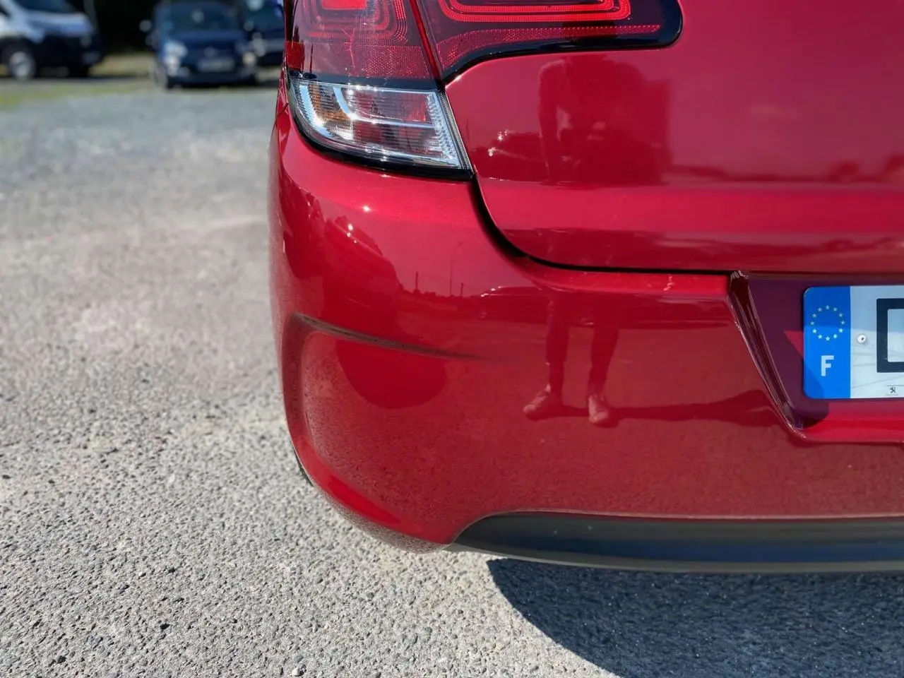Gros plan sur le coin arrière gauche rouge métallisé d'une Citroën C4 Millenium avec feu arrière et plaque d'immatriculation française visible.