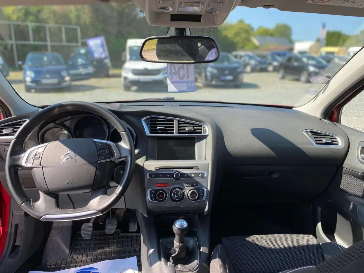 Intérieur avant d'une Citroën C4 rouge 2015, vue du poste de conduite avec tableau de bord et boîte manuelle visible.