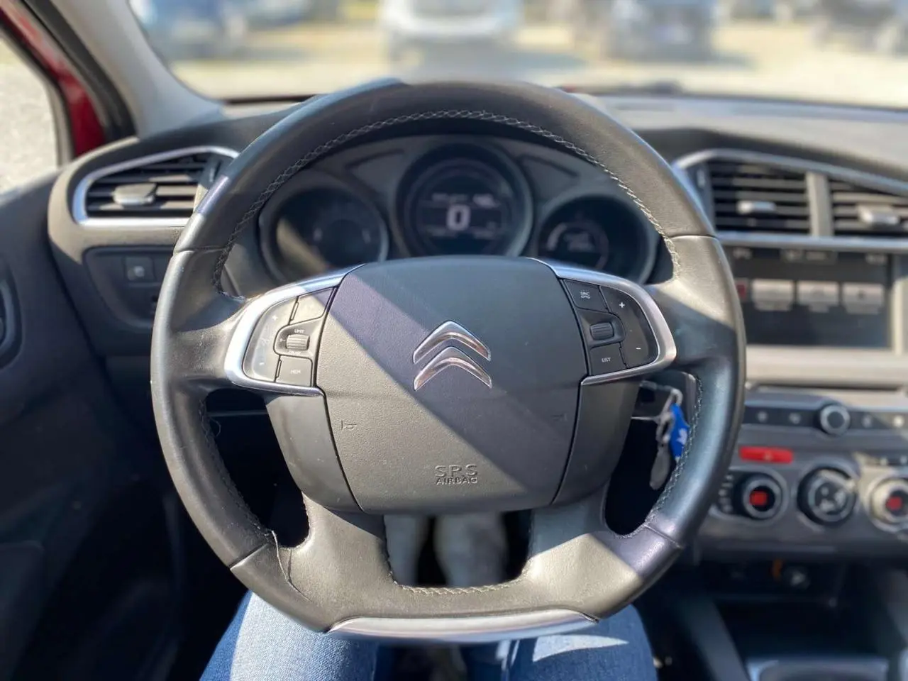 Vue rapprochée du volant cuir noir de la Citroën C4 Millenium 2015 avec commandes intégrées et tableau de bord flou.