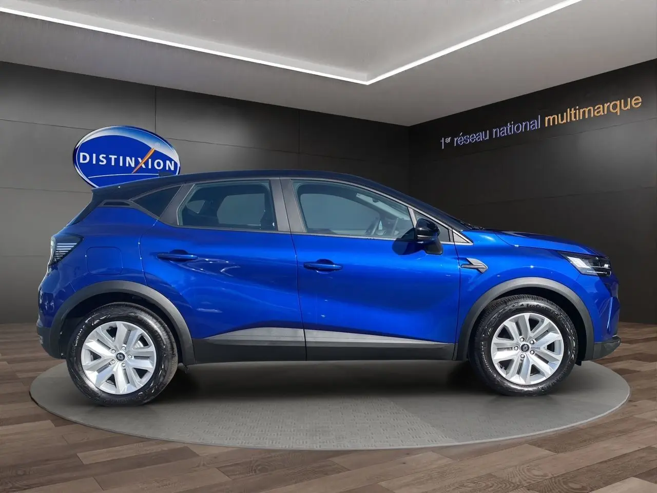 Renault Captur TCE 90 Evolution 2024 en bleu iron avec toit noir, vue profil côté gauche en intérieur showroom.
