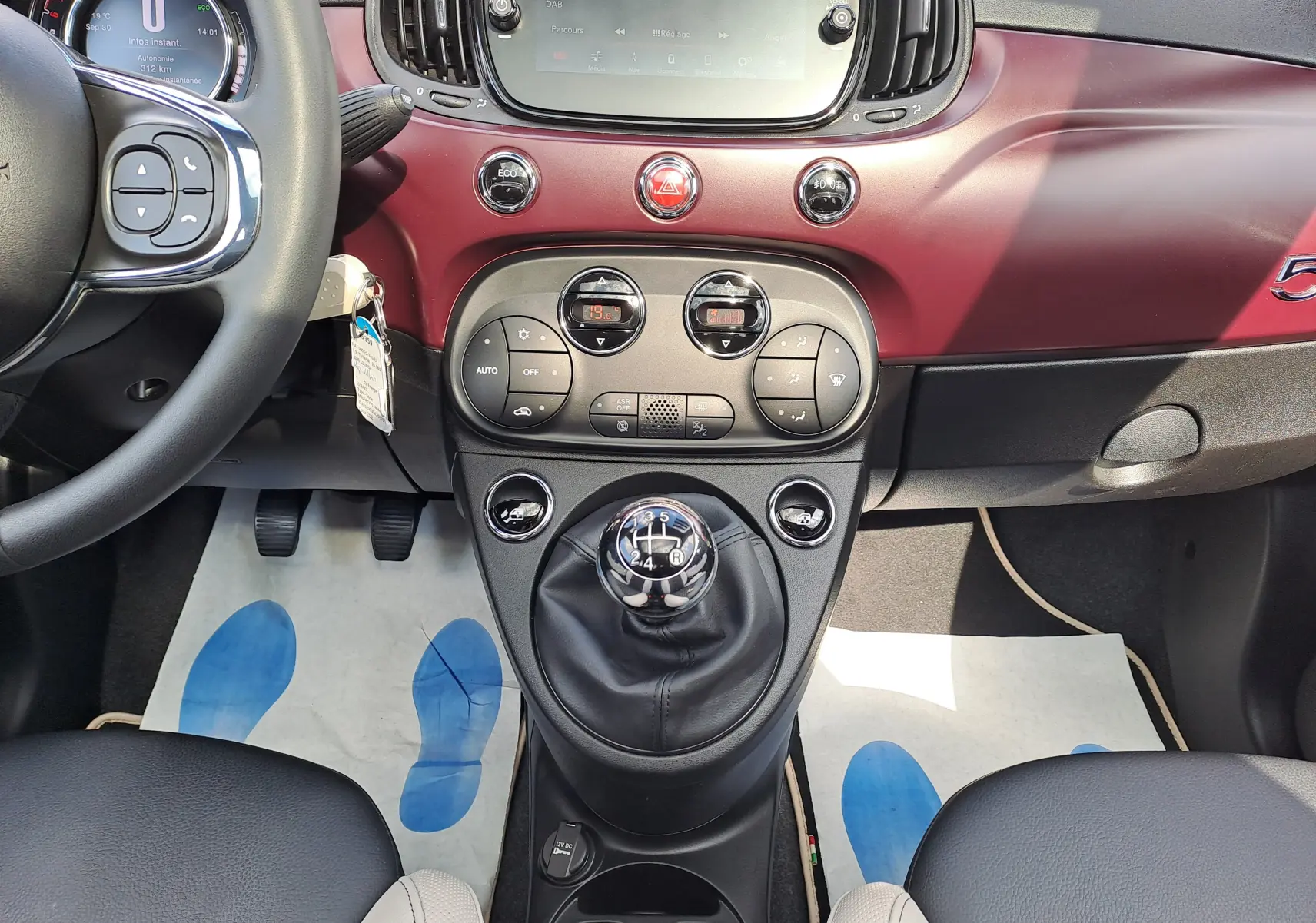 Vue intérieure centrale de la Fiat 500 2020 avec tableau de bord bordeaux et levier de vitesse manuel visible.