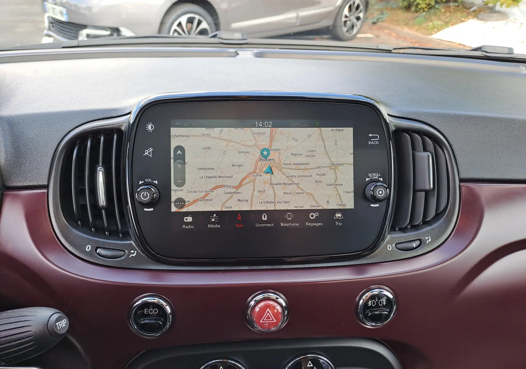 Tableau de bord bordeaux de Fiat 500 2020 avec écran tactile affichant la navigation et commandes centrales visibles.