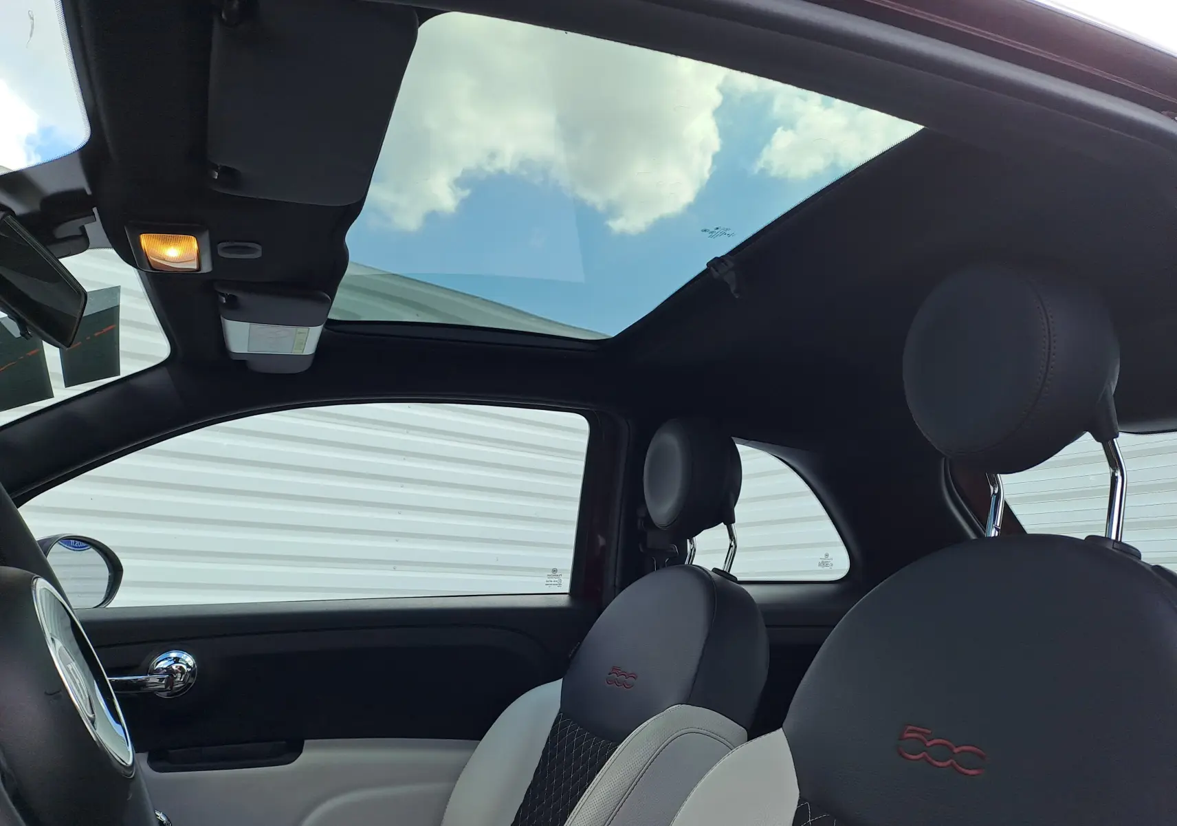 Vue intérieure côté conducteur de la Fiat 500 Opera Bordeaux avec toit panoramique et sièges noirs brodés du logo 500 rouge.