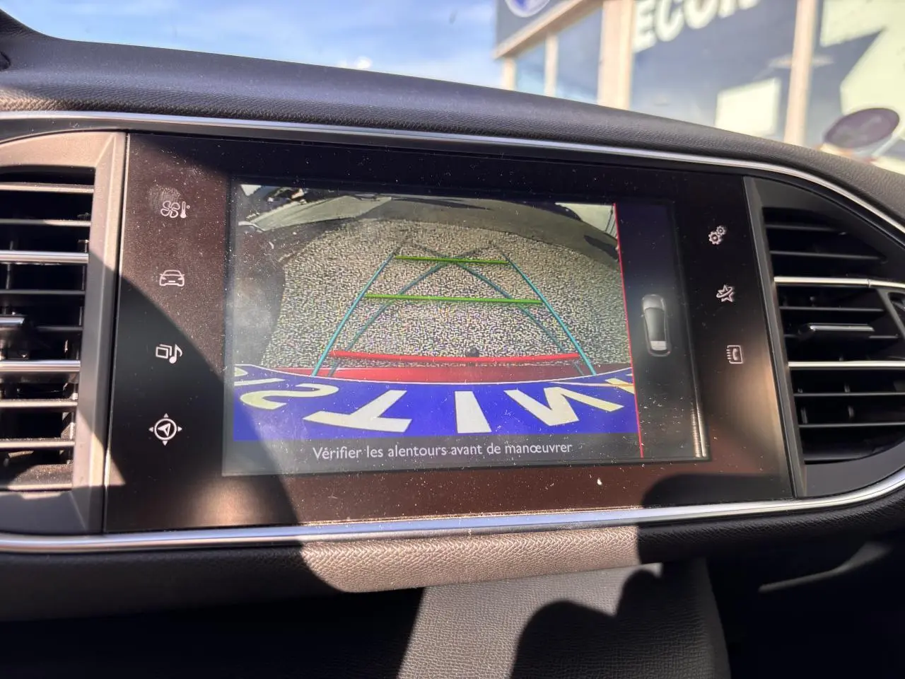 Écran tactile intérieur affichant la caméra de recul d'une Peugeot 308 GT Line rouge foncé, avec lignes de guidage colorées.