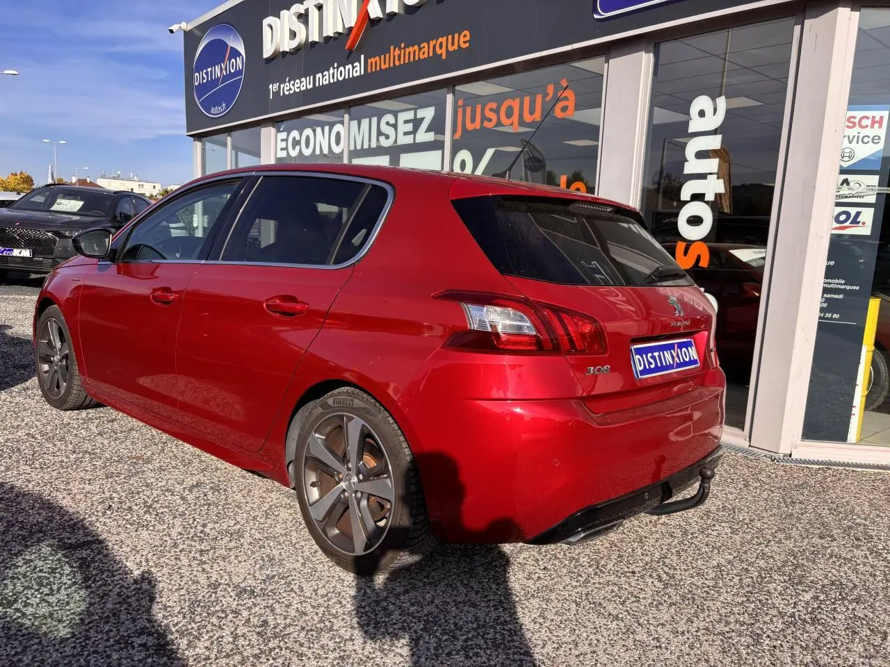 Vue 3/4 arrière droite d'une Peugeot 308 GT Line rouge foncé avec jantes diamantées et toit panoramique stationnée devant un showroom
