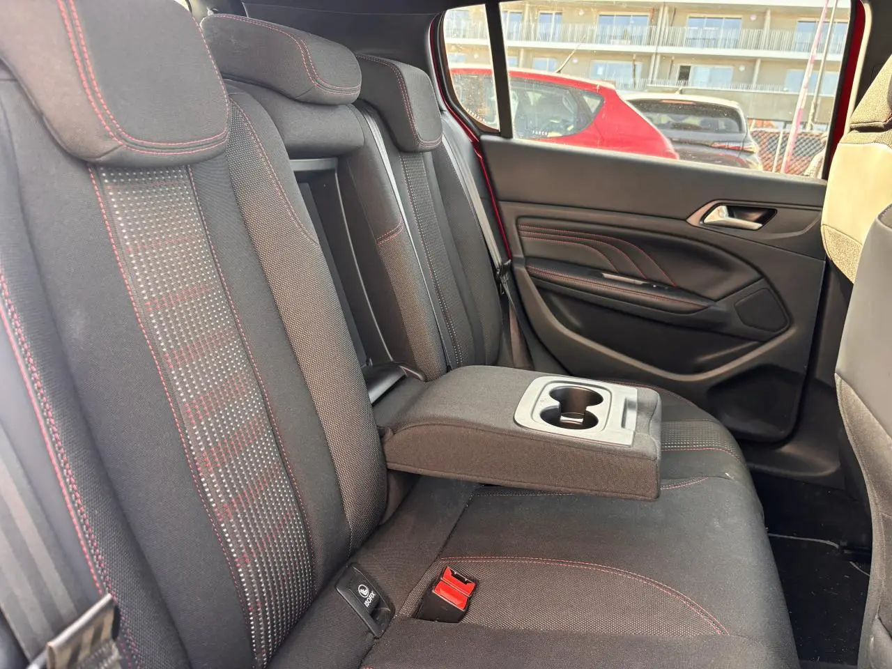 Vue côté droit de la banquette arrière noire avec surpiqûres rouges et accoudoir central déployé d'une Peugeot 308 rouge foncé.