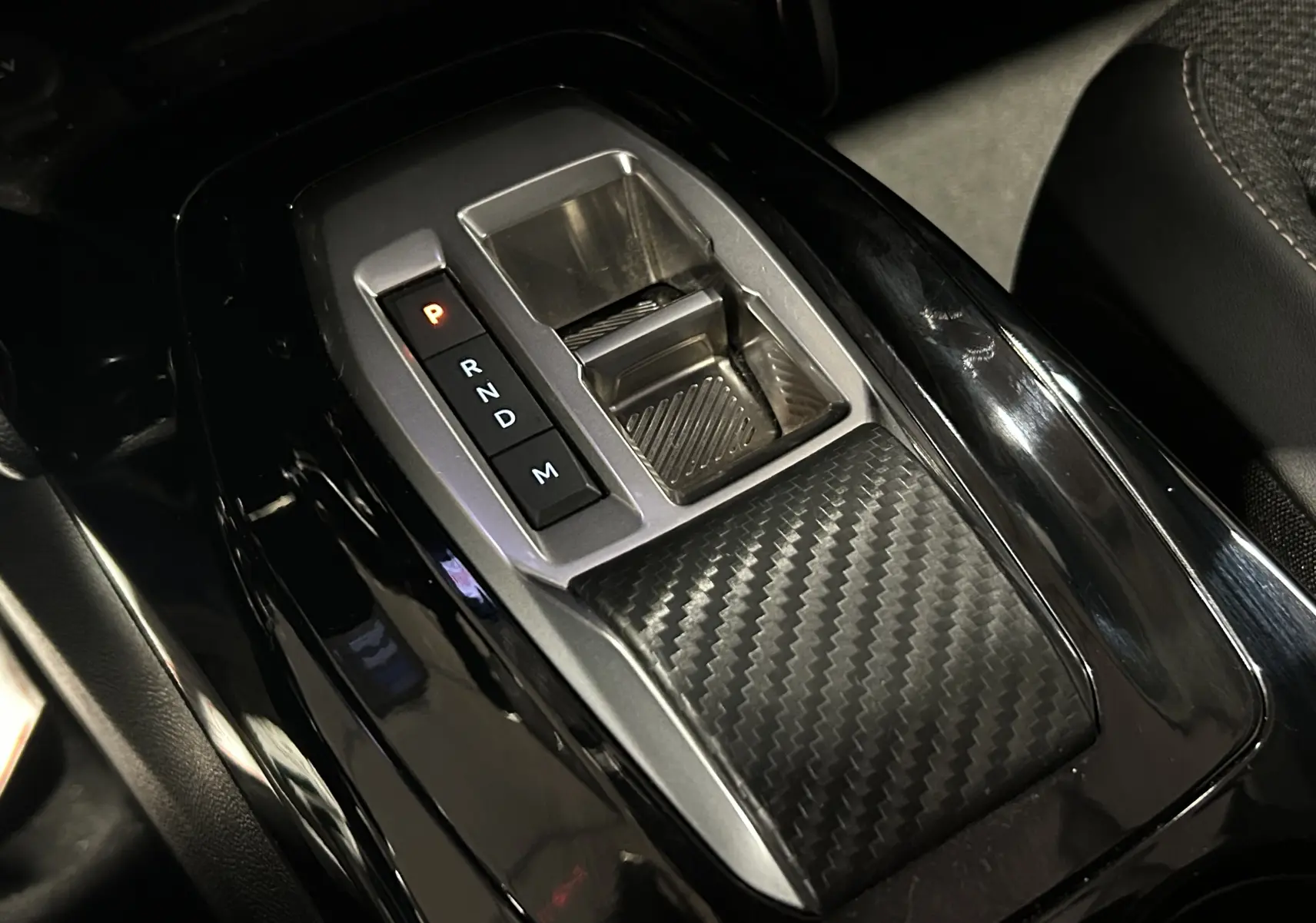 Gros plan sur la console centrale noire brillante du Peugeot 2008 Allure Hybrid 145 avec levier de vitesses automatique et insert carbone.