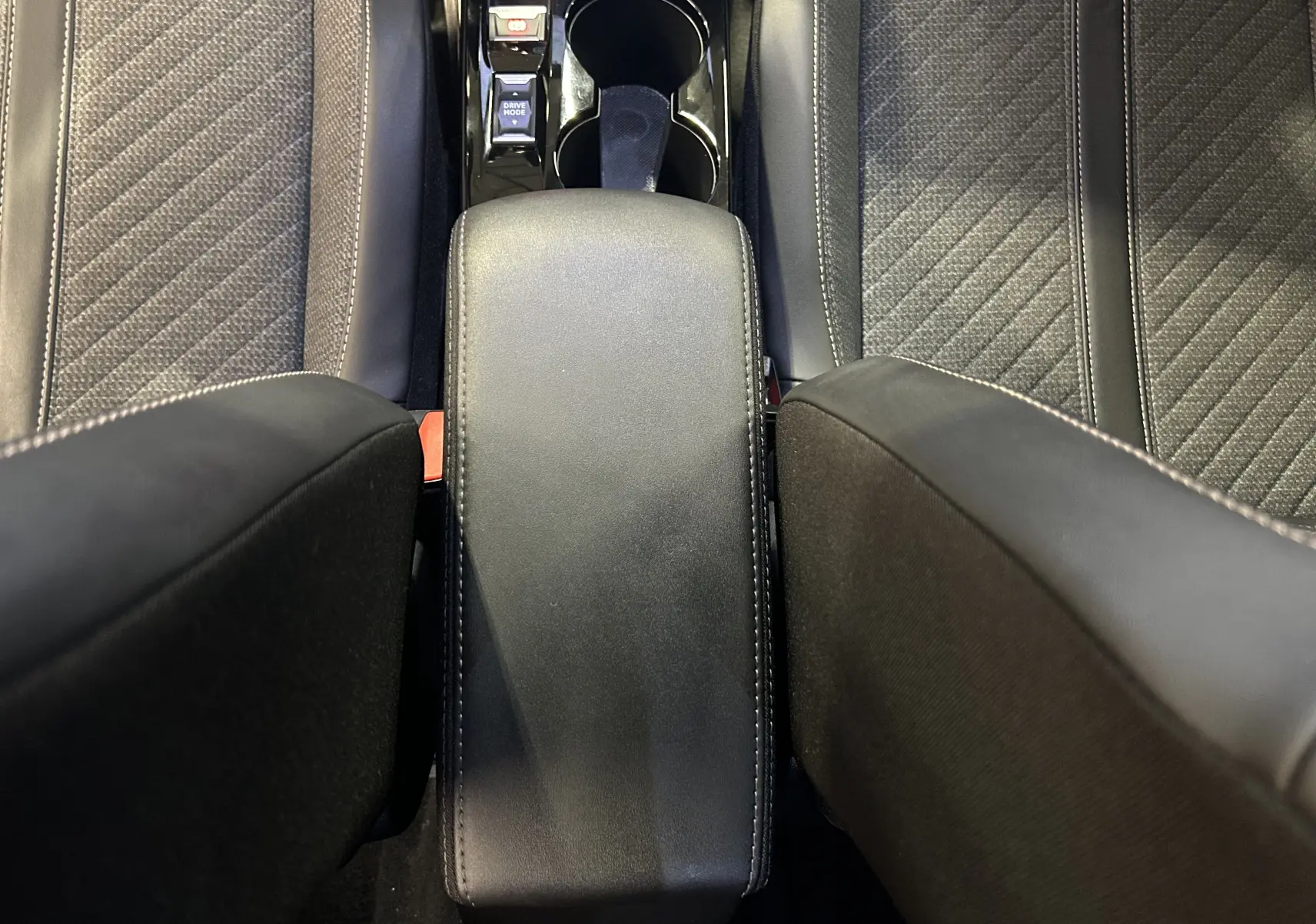 Vue plongeante sur l'accoudoir central en cuir noir et les sièges gris à surpiqûres du Peugeot 2008 Allure Hybrid 2025.