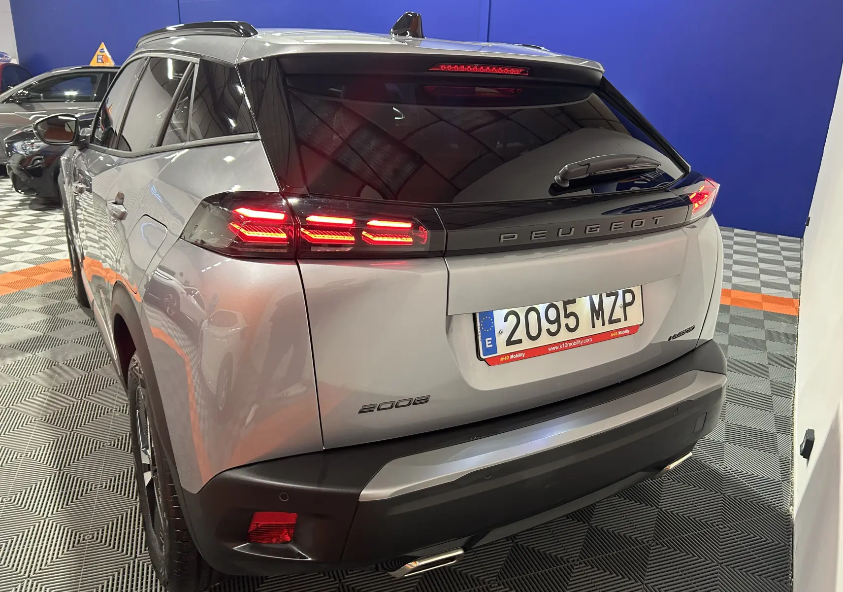 Vue 3/4 arrière droite d'un Peugeot 2008 gris hybride avec feux arrière LED allumés en intérieur showroom.